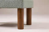 Close-up of two round walnut-stained wood legs under the corner of the boucle seat