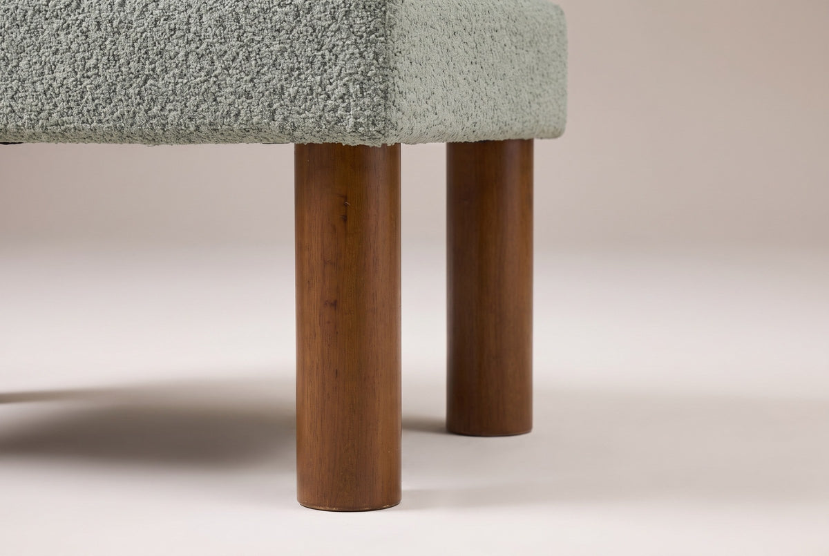 Close-up of two round walnut-stained wood legs under the corner of the boucle seat