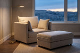 Faenza chair and ottoman in a Calgary family room at dusk, a brass floor lamp lit and the foothills through the window