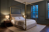 Fermo canopy bed in a dark green panelled bedroom at dusk, a lamp glowing on a walnut nightstand