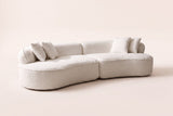 The Fiora curved sofa in White, front three-quarter view: a long, low kidney-shaped boucle sofa in two pieces with throw pillows, on an off-white studio background