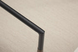 Close-up of a black steel arm tube bending down into its short black sleeve on the bronze leg, over the slub-weave seat