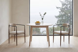 Two Fiuggi chairs either side of a round oak table in a Vancouver dining nook, a misty sea and evergreens through the window