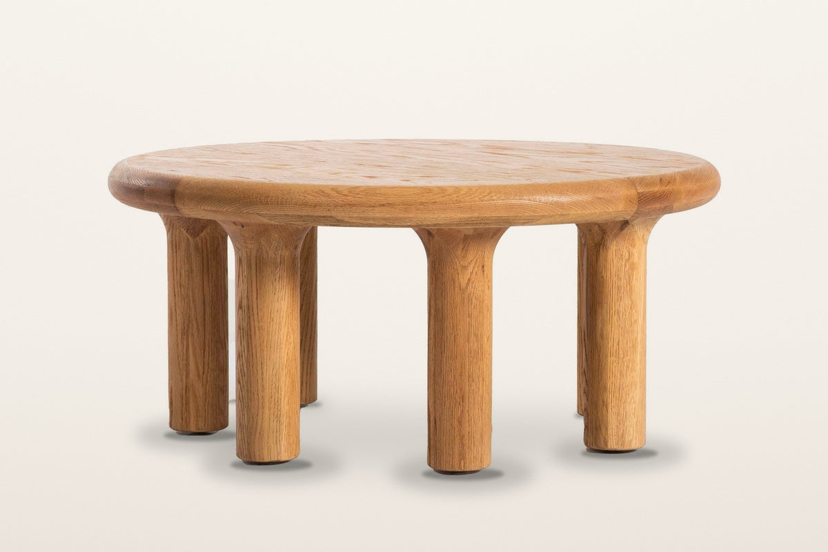 Fontanellato coffee table in Natural Oak, front view on a warm white studio backdrop: each pillar leg flares into the undersi