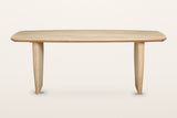 Frontino dining table in Biscotti Oak, straight front view on a warm white studio backdrop: the long boat-shaped top on two s
