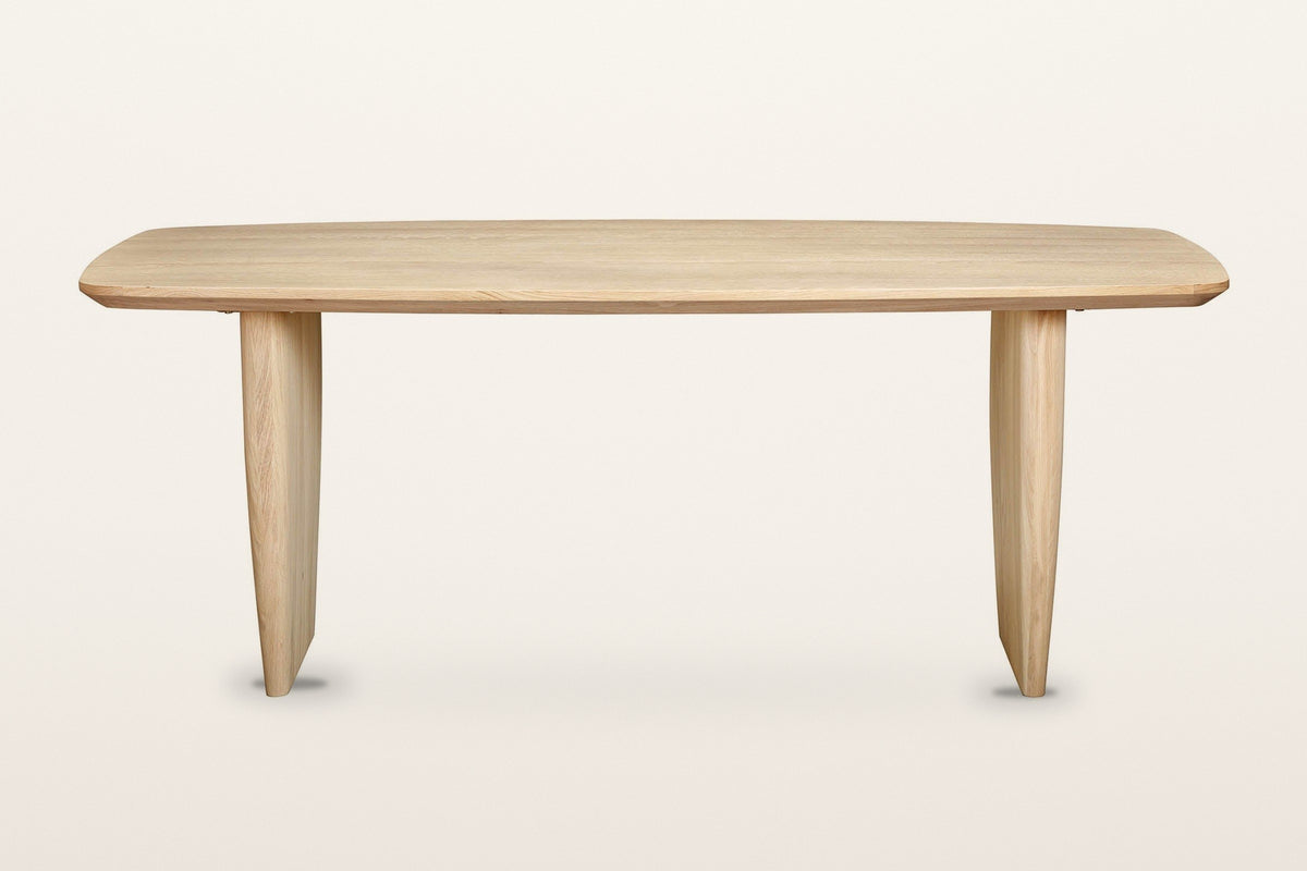 Frontino dining table in Biscotti Oak, straight front view on a warm white studio backdrop: the long boat-shaped top on two s