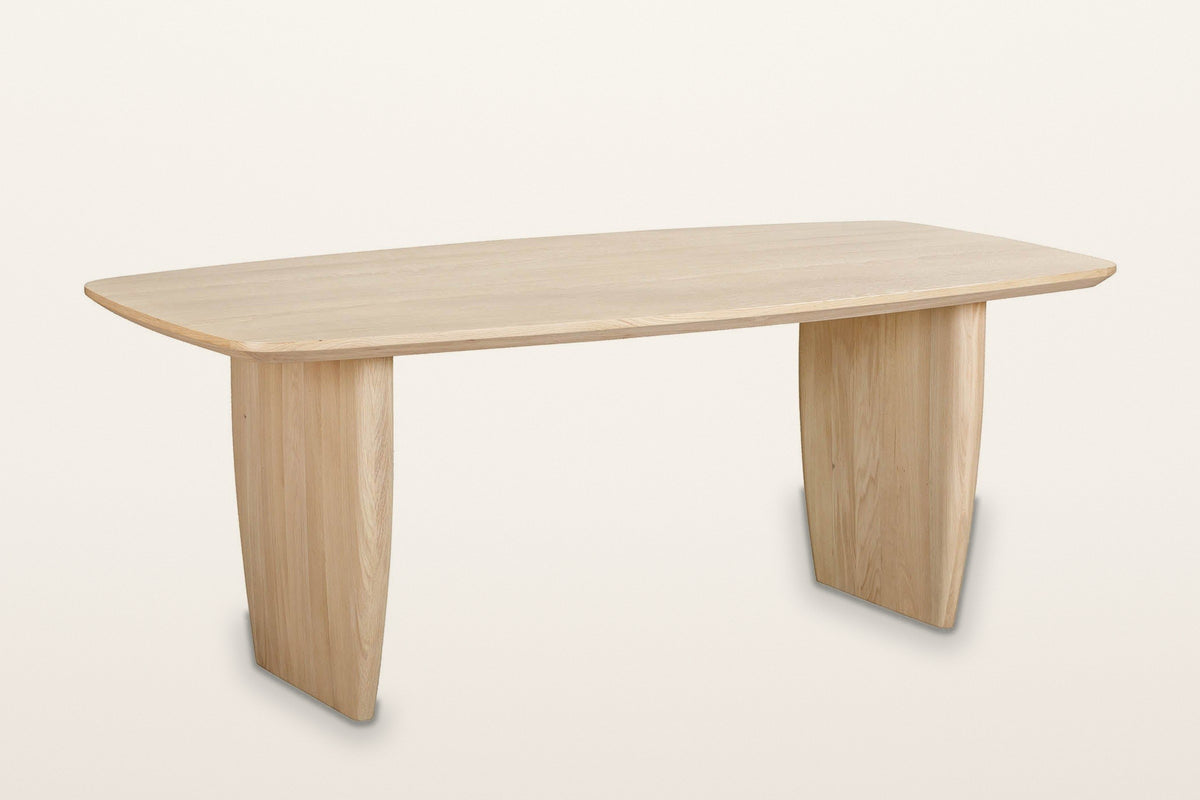 Frontino slab-leg oak dining table in Biscotti Oak, three-quarter view on a warm white studio backdrop
