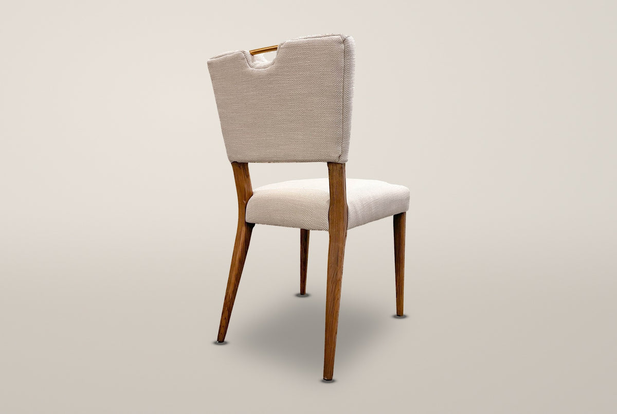 The Galen chair from behind at an angle, showing the thin back panel, the notch with its brass-tone bar and the angled rear legs