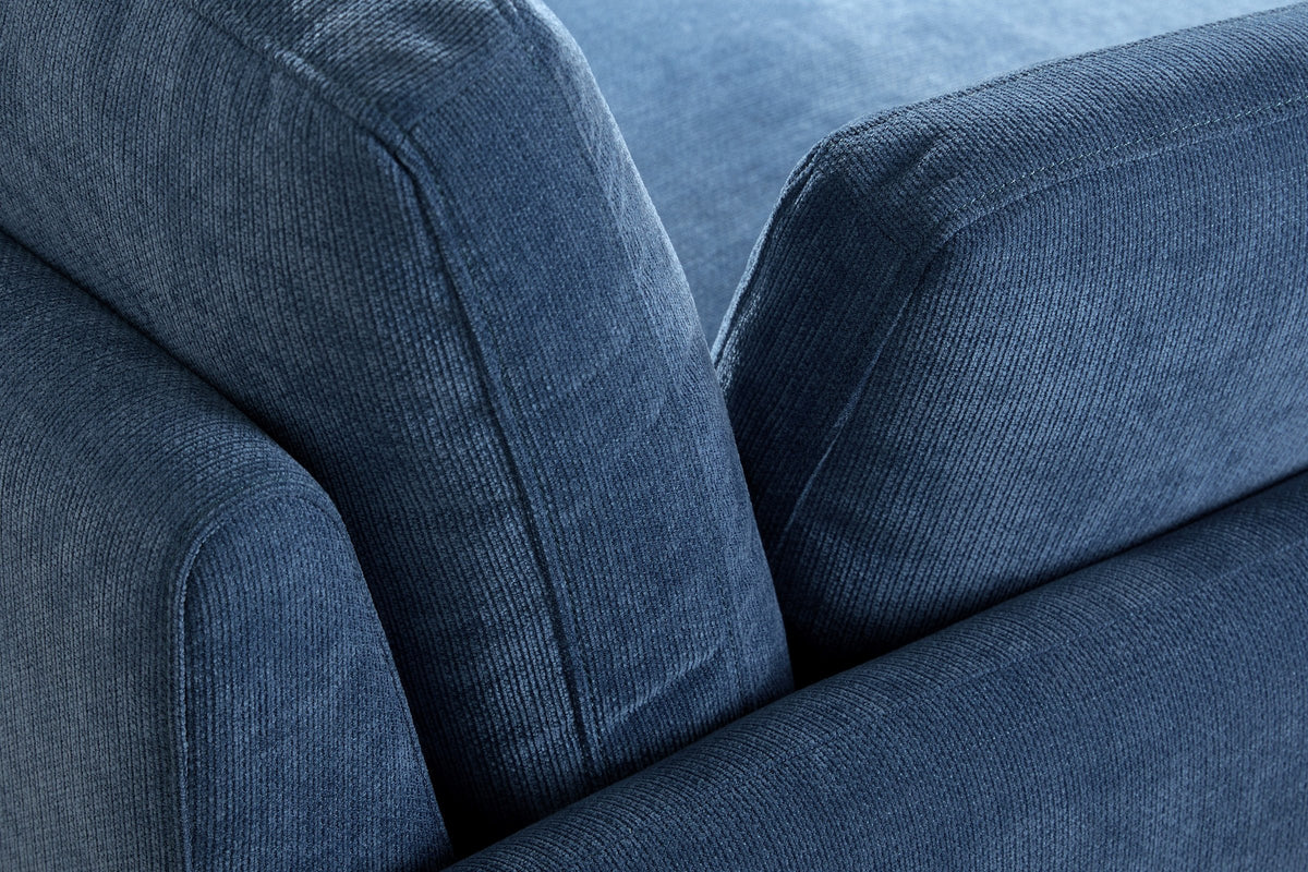 Close-up of the ribbed denim blue chenille where the arm, the back cushion and a pillow meet, with their top-stitched edges