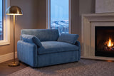 Gallipoli chair in denim blue in a Calgary family room at dusk, beside a limestone fireplace and a lit brass floor lamp