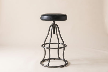 Garrick adjustable bar stool in Black, three-quarter view on a warm off-white studio backdrop: a black leather seat on the gu