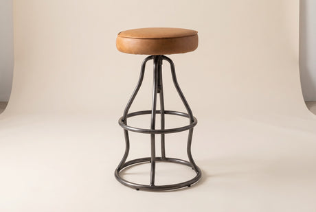 Garrick adjustable bar stool in Cognac, three-quarter view on a warm off-white studio backdrop: a tan leather seat on the gun