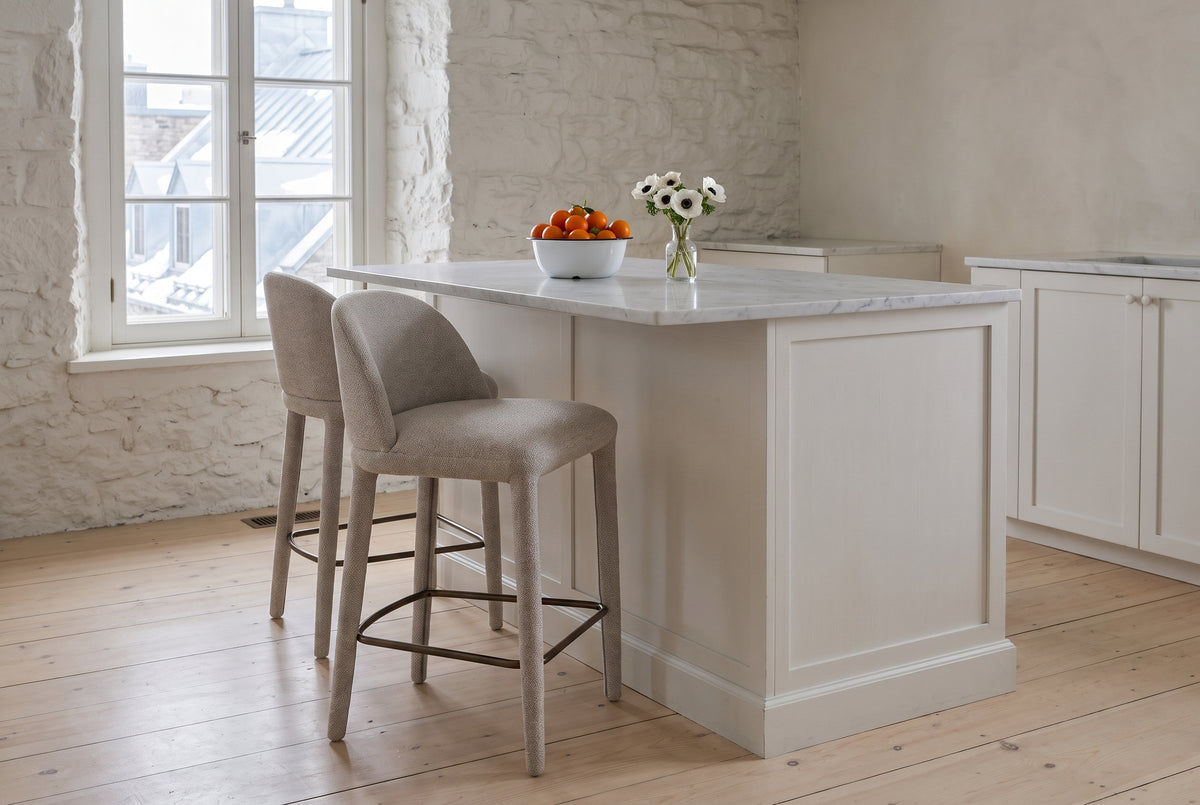 Two Gavi counter stools in beige at a white marble kitchen island in an old stone house in Quebec City