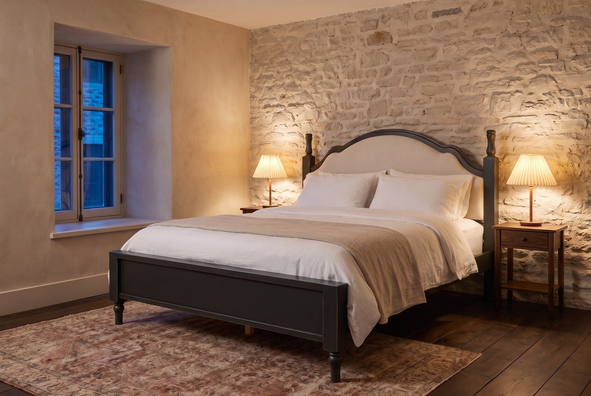Gradara bed in black against a pale limestone wall at dusk, with pleated lamps lit on two walnut nightstands