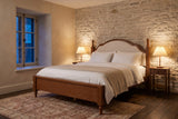 Gradara bed against a pale limestone wall at dusk, with pleated lamps lit on two walnut nightstands