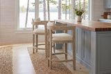 Two Gradisca counter stools in Natural Ash at a butcher-block island in a Muskoka cottage kitchen with a window onto the lake