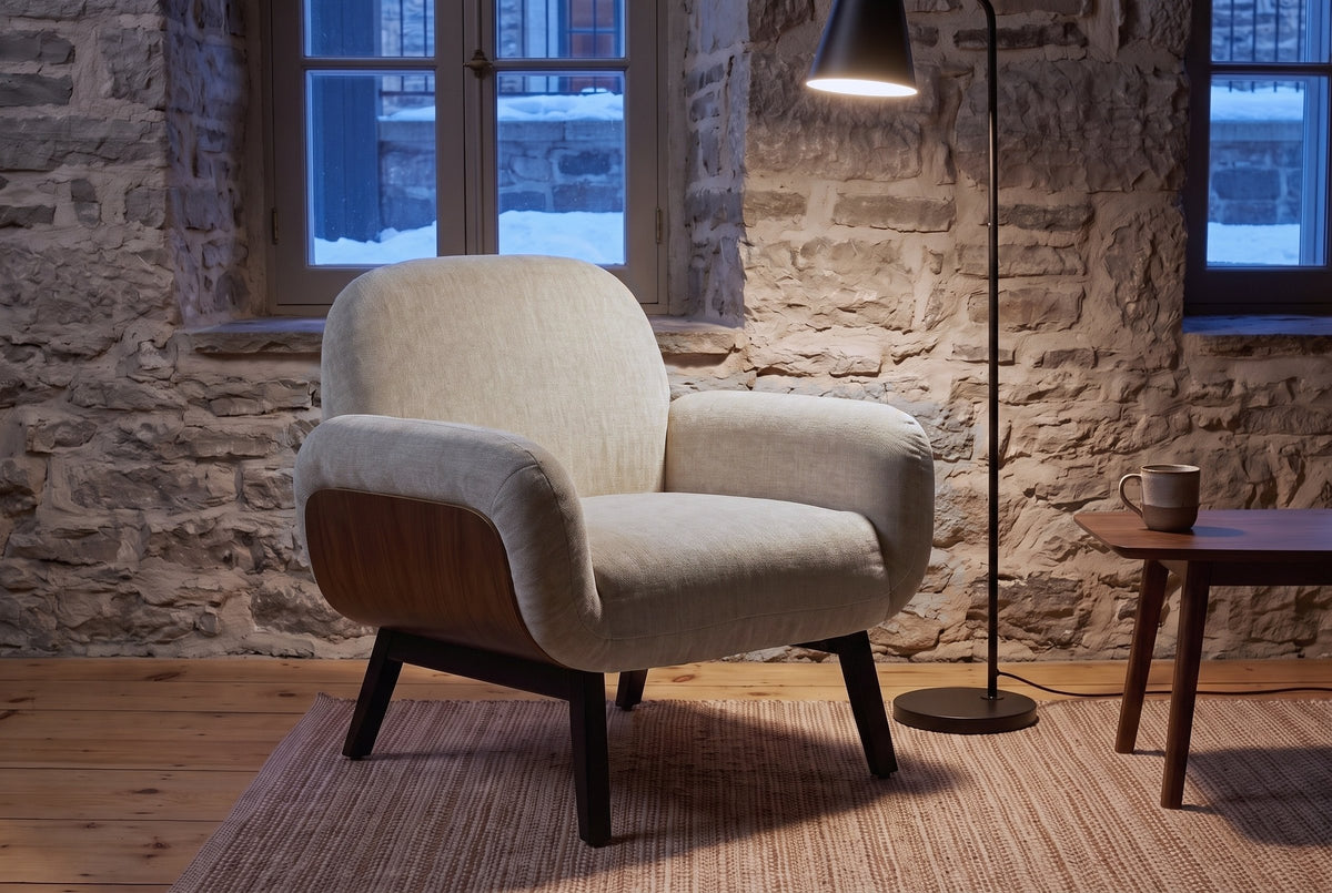 Grado chair in oat against a fieldstone wall in a Quebec City sitting room at dusk, a black floor lamp lit beside it