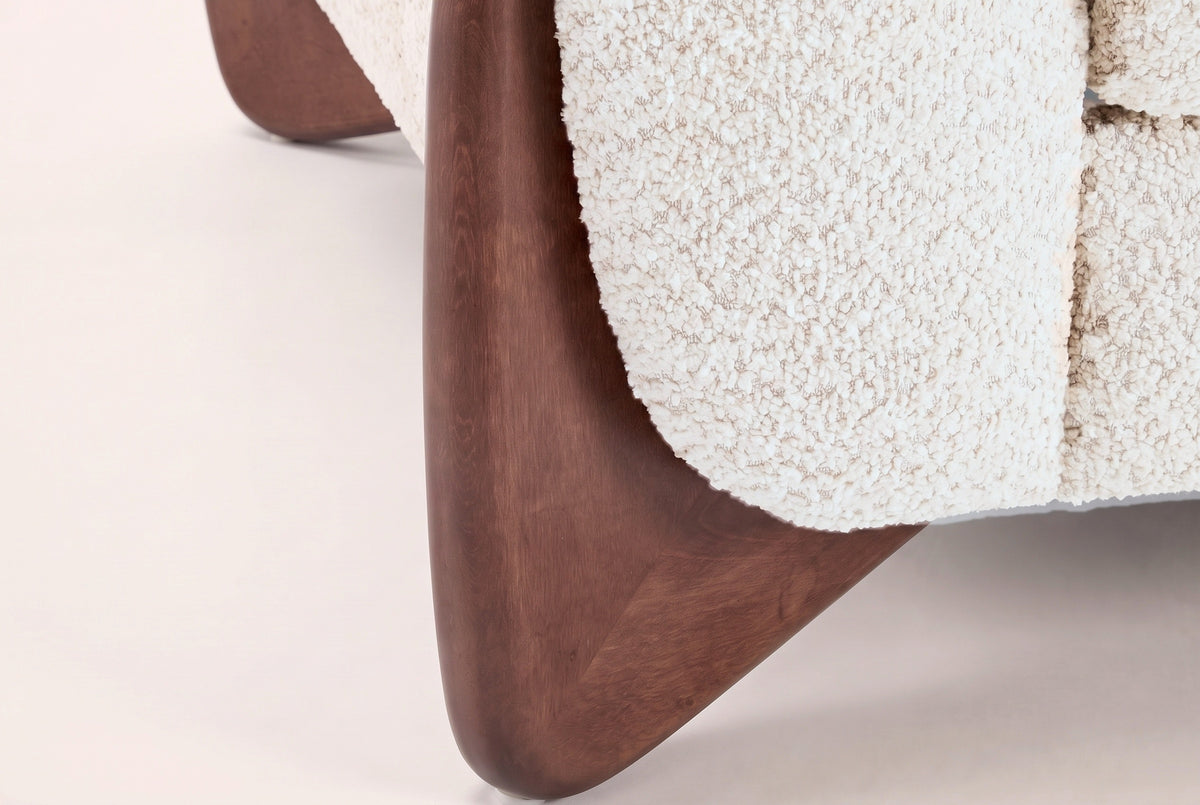 Close-up of a solid birch wedge leg in a walnut-brown stain under the beige boucle arm