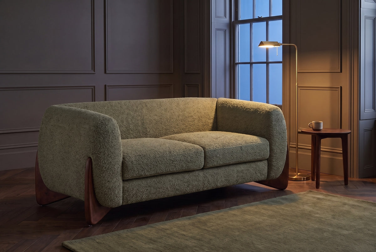 Greccio boucle loveseat in olive green in a dark panelled townhouse sitting room at dusk, a brass floor lamp lit beside it
