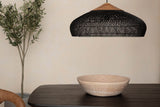 Halden black rattan pendant light hanging over a dark wood dining table