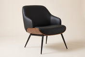 Iver accent chair in Black / Walnut, three-quarter view on a warm off-white studio backdrop: a curved black faux leather shel