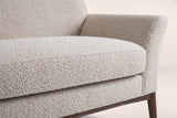 Close-up of the almond boucle seat cushion, the flared arm and a tapered walnut-finish leg