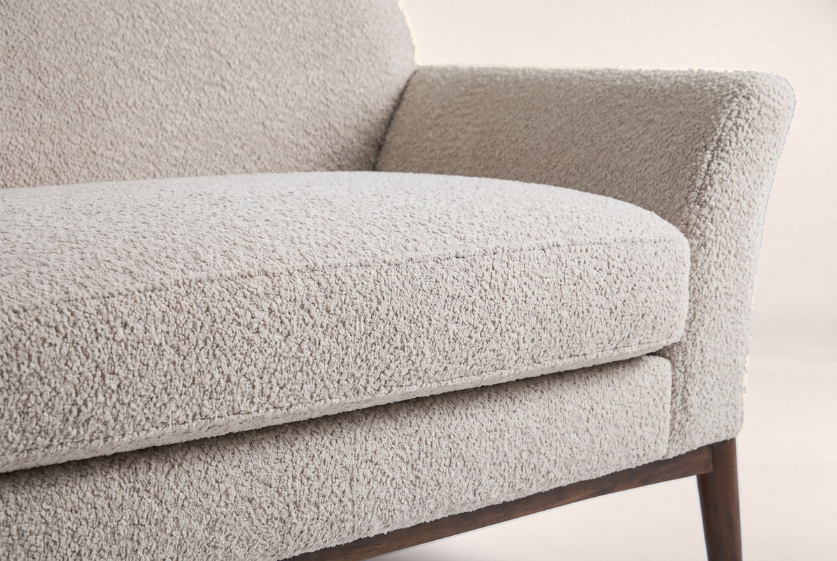 Close-up of the almond boucle seat cushion, the flared arm and a tapered walnut-finish leg