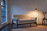 Jesi loveseat against a whitewashed brick wall in a Montreal loft at dusk, a brass floor lamp lit beside it