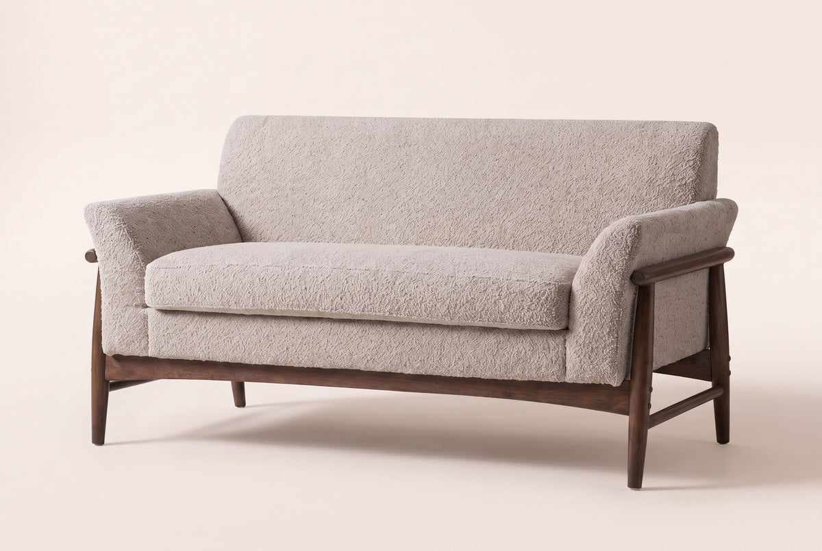 Jesi flared-arm loveseat in almond boucle on a walnut-finish wood frame, three-quarter view on a warm cream studio backdrop