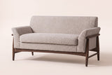 Jesi flared-arm loveseat in almond boucle on a walnut-finish wood frame, three-quarter view on a warm cream studio backdrop