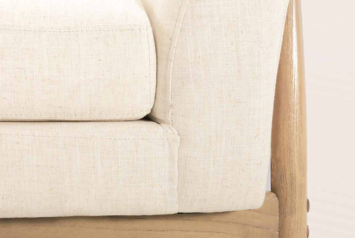 Close-up of the beige woven seat cushion and flared arm, with the natural-finish wooden side frame and its round wooden bolt plugs