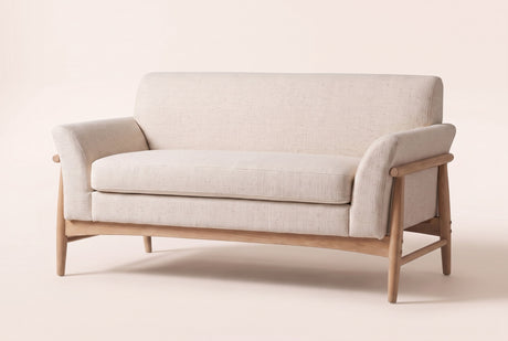 Jesi flared-arm loveseat in beige woven fabric on a natural-finish wood frame, three-quarter view on a warm cream studio backdrop