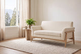 Jesi loveseat in beige woven fabric on a natural-finish frame in a bright Vancouver living room with a travertine side table, a fern and a window onto cedars and mountains