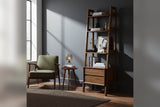 Keaton Warm Pecan bookcase styled with books beside a green armchair in a grey room