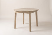 Keaton solid acacia round dining table in Light Driftwood, three-quarter view on a warm off-white studio backdrop