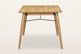 End view of the Larino dining table in Natural on a warm white studio backdrop: two splayed legs and the forked rod
