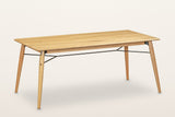 Larino oak dining table in Natural, three-quarter view on a warm white studio backdrop: four splayed legs and thin black rods