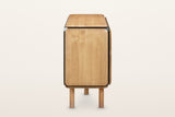 The end of the Larino sideboard in Natural and Black on a warm white studio backdrop: a rounded oak end framed in black