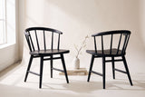 Two Lauryn dining chairs in black oak, one seen from the front and one from behind, with a blossom branch in a white vase on stone slabs between them