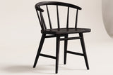One black oak Lauryn dining chair on an off-white backdrop, seen from the front three-quarter: the curved back rail with rounded tips, the slim spindles, the carved seat and the four splayed legs with their stretchers