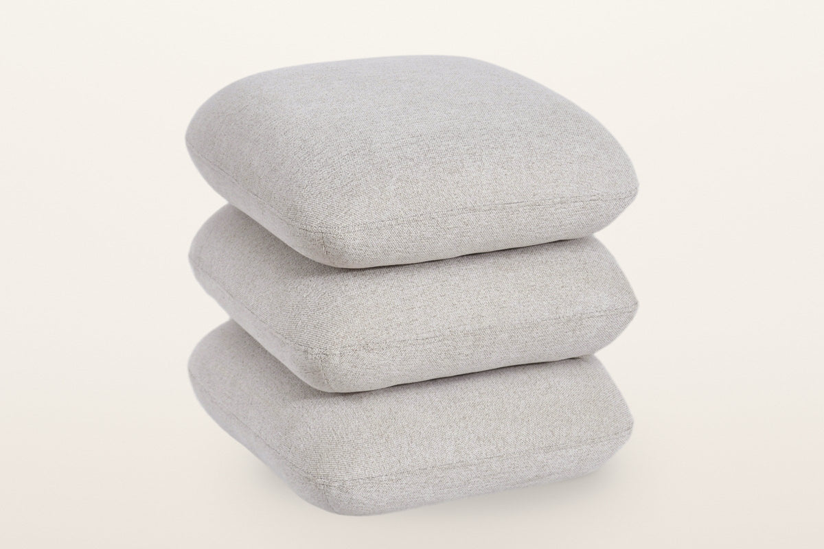 Lavagna square ottoman in Beige, three-quarter view on a warm white studio backdrop: three soft square pillows stacked one on another