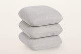 Lavagna square ottoman in Beige, three-quarter view on a warm white studio backdrop: three soft square pillows stacked one on another