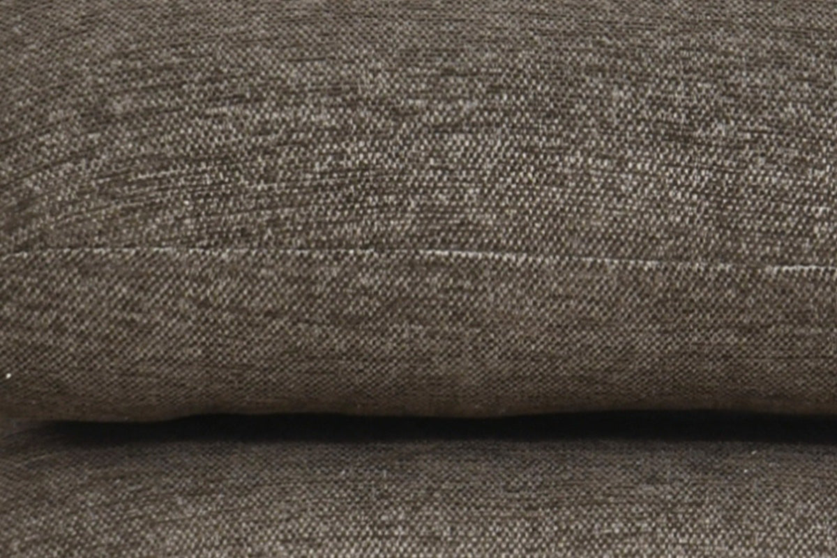 Close-up of the Lavagna ottoman in Brown: a pillow's rounded edge and its one fine seam over the pillow below