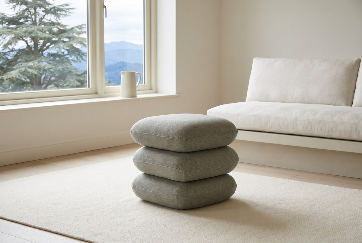 A Lavagna ottoman in Sage on an ivory rug in a Craftsman bungalow living room in Kitsilano, Vancouver, an off-white linen sofa behind and a cedar and mountains through the window