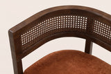 Close-up of the woven rattan back between its two wooden rails, the squared arm end and the dark orange seat pad