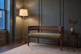 Levanto loveseat in green and walnut against a green-grey panelled wall in a Toronto townhouse at dusk, a brass floor lamp lit beside it