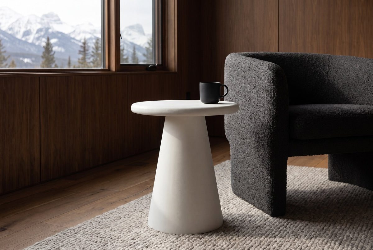 Levico round white side table beside a charcoal boucle chair in a walnut-panelled Canmore living room, mountains through the window