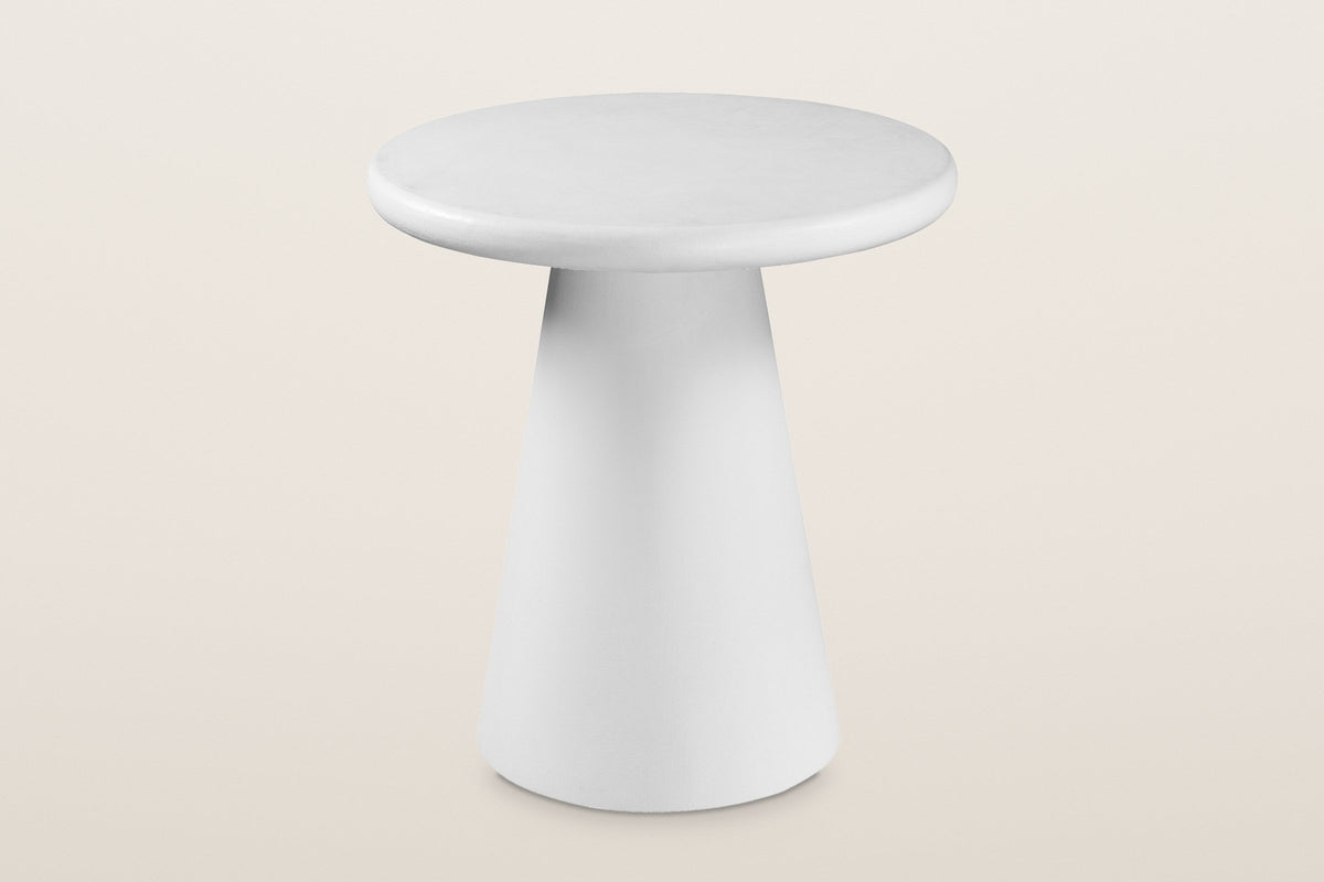 Levico round side table in matte white with a cone pedestal, three-quarter view on a warm light studio backdrop