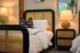 Linden lamp glowing on a cane nightstand beside a bed