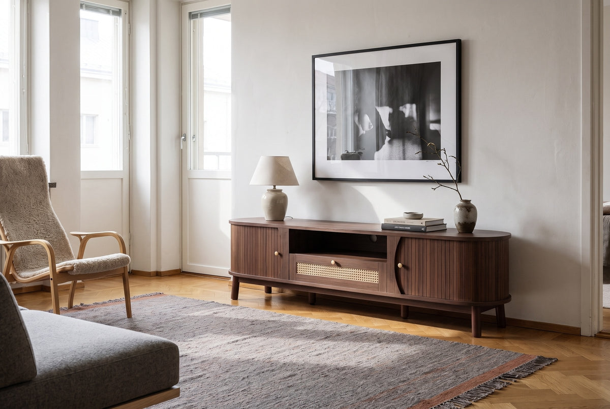 The Livia media console in Natural Walnut below a framed black-and-white photograph, in a Helsinki apartment with a parquet floor, a birch lounge chair and a grey sofa